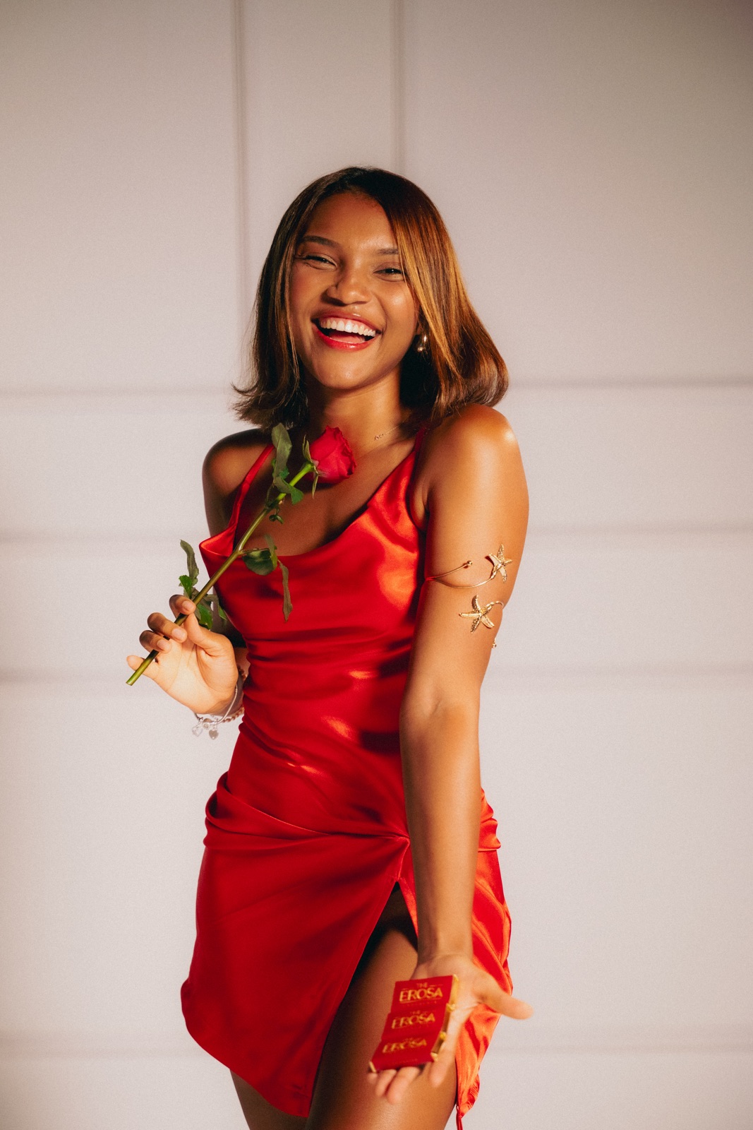 A woman in a red satin dress with a rose, holding out an Erosa pack