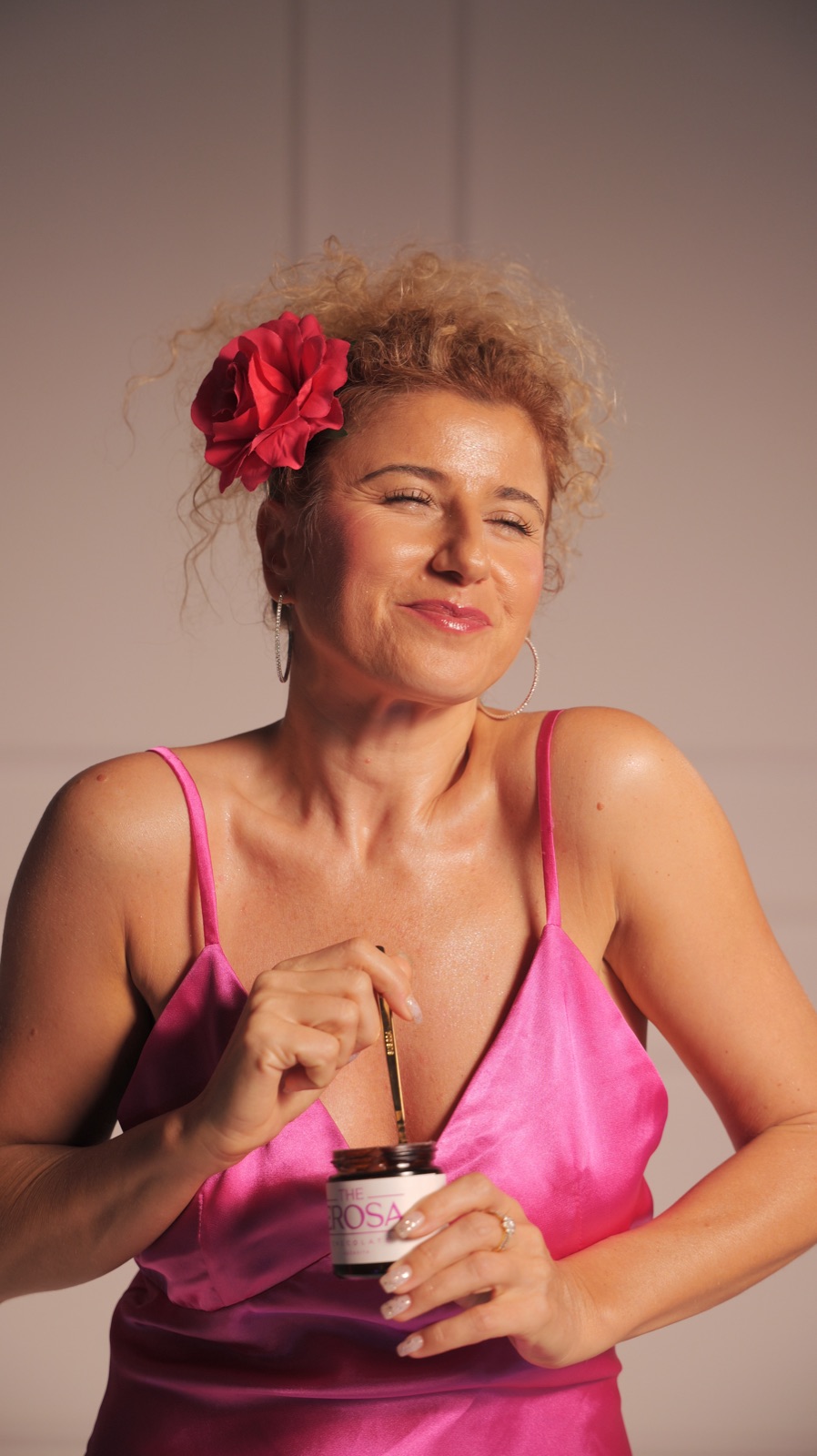 A woman in pink with a red flower in her hair, eating from a jar of Erosa
