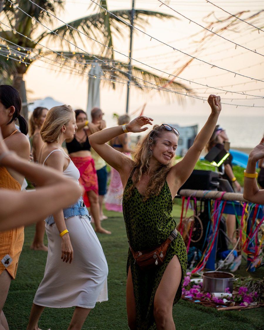 Guests dancing on the grass at an Extaticaa event, with palm trees and the sea behind them